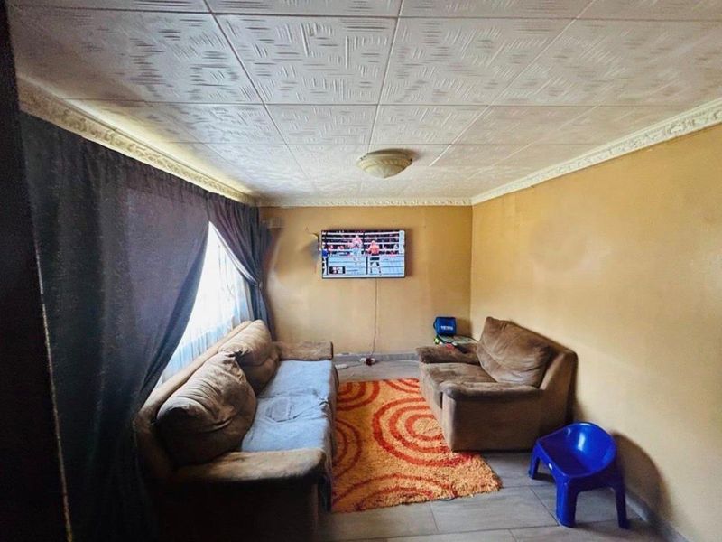A living room featuring textured ceiling tiles, decorative cornice, and tiled flooring, currently requiring cosmetic updates to the wall finishes.