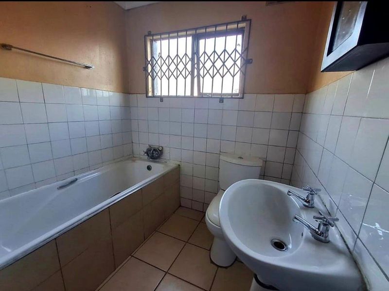 A functional bathroom featuring a bathtub, pedestal basin, and toilet, finished with tiled walls and flooring, requiring cosmetic updates.