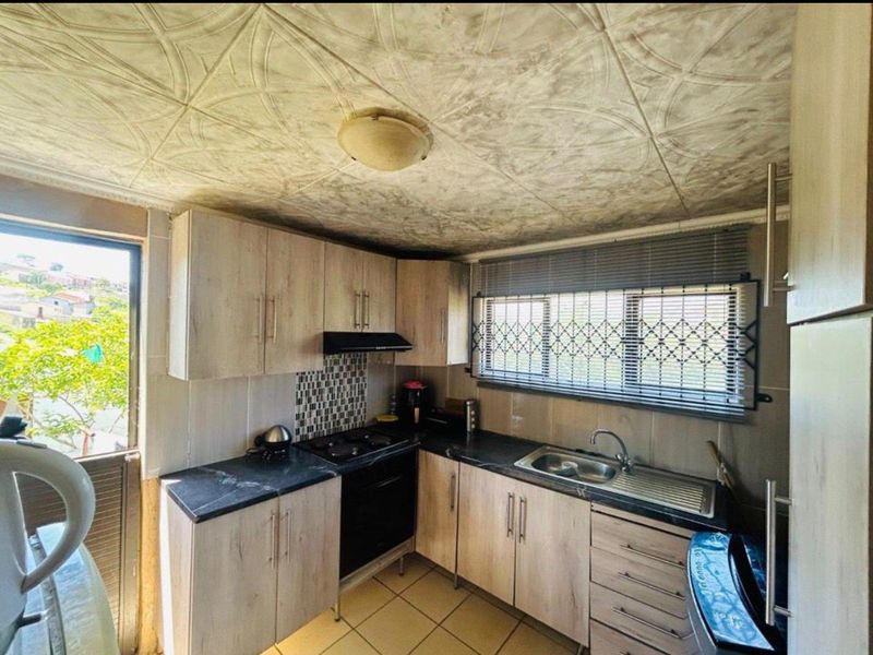 Compact kitchen featuring light wood-finish cabinetry, dark laminate countertops, built-in oven with extractor, and tiled flooring with direct access to the exterior.