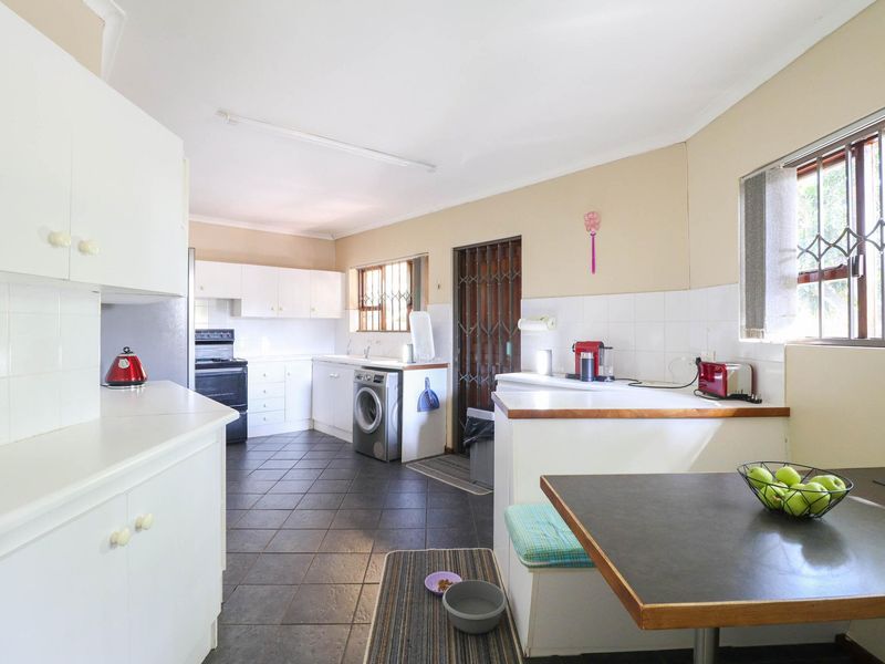 A functional kitchen featuring white cabinetry, tiled flooring, a tiled backsplash, and integrated appliances, offering a practical layout with direct access to the exterior.