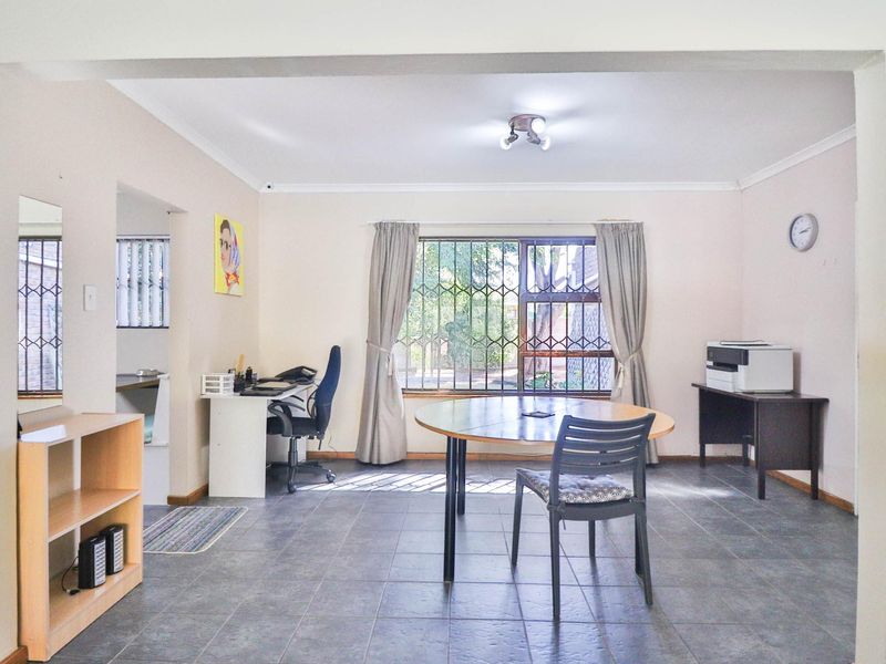 A spacious living area featuring tiled flooring, security bars on the windows, and neutral wall finishes, offering a versatile space for various uses.