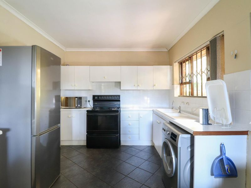 Functional kitchen featuring white cabinetry, tiled splashbacks, a double sink, and tiled flooring, with space for a washing machine and freestanding stove.