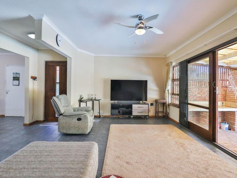 Spacious living room featuring tiled flooring, a ceiling fan, and large sliding glass doors providing direct access to the outdoor patio area.