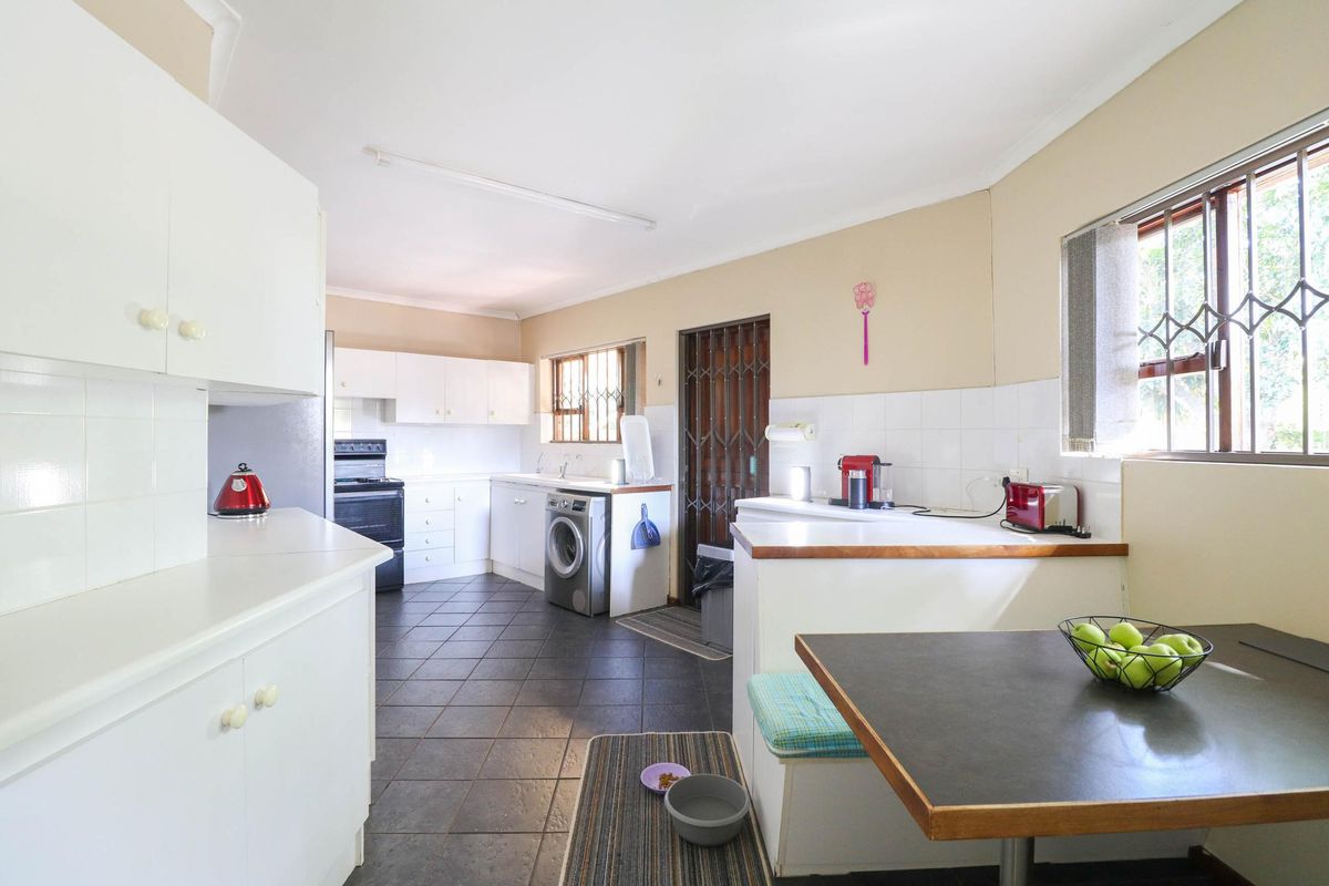 A functional kitchen featuring white cabinetry, tiled flooring, a tiled backsplash, and integrated appliances, offering a practical layout with direct access to the exterior.
