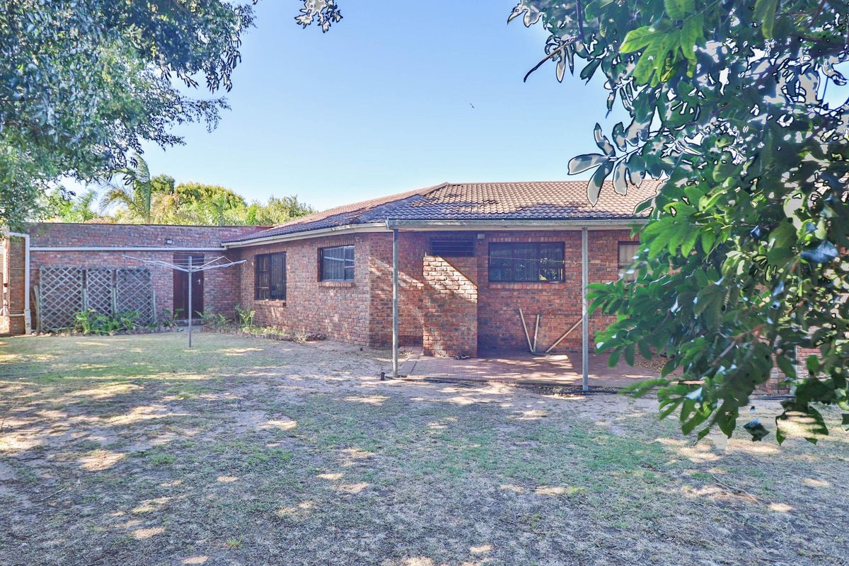 Rear view of the property featuring a brick facade, tiled roof, and a covered patio area overlooking the garden.
