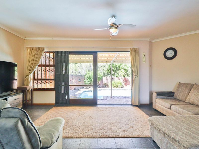 Spacious living room featuring tiled flooring, a ceiling fan, and large sliding glass doors providing direct access to the outdoor patio and pool area.