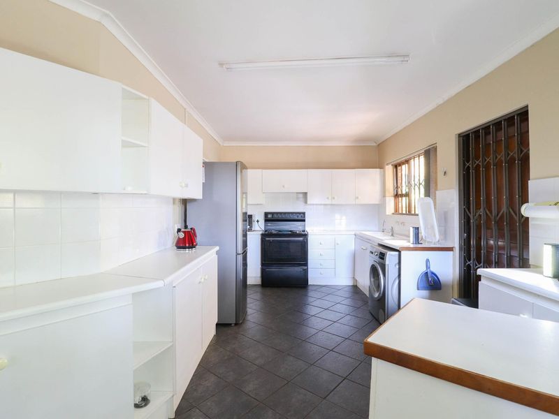 A functional kitchen featuring white cabinetry, dark tiled flooring, a tiled backsplash, and a freestanding stove, with a security gate at the side entrance.