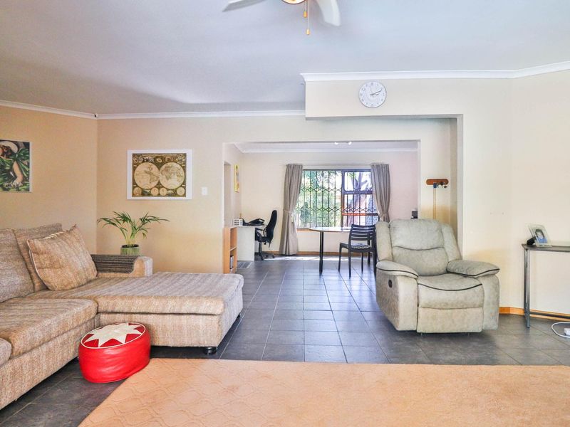 Spacious open-plan living area featuring tiled flooring, a ceiling fan, and large windows with security bars, offering a versatile layout for dining and relaxation.