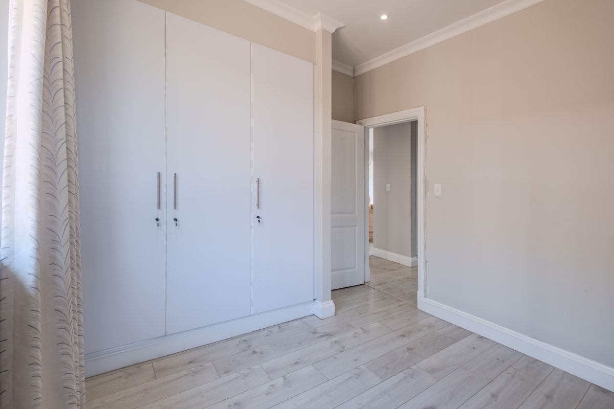 A bright, neutral bedroom featuring modern laminate flooring, built-in cupboards, and clean finishes, offering a versatile space ready for personalization.