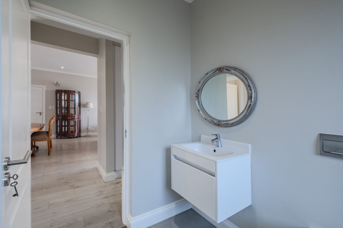 A modern, minimalist guest bathroom featuring a wall-mounted vanity with a basin and a sleek wall-mounted toilet flush plate.