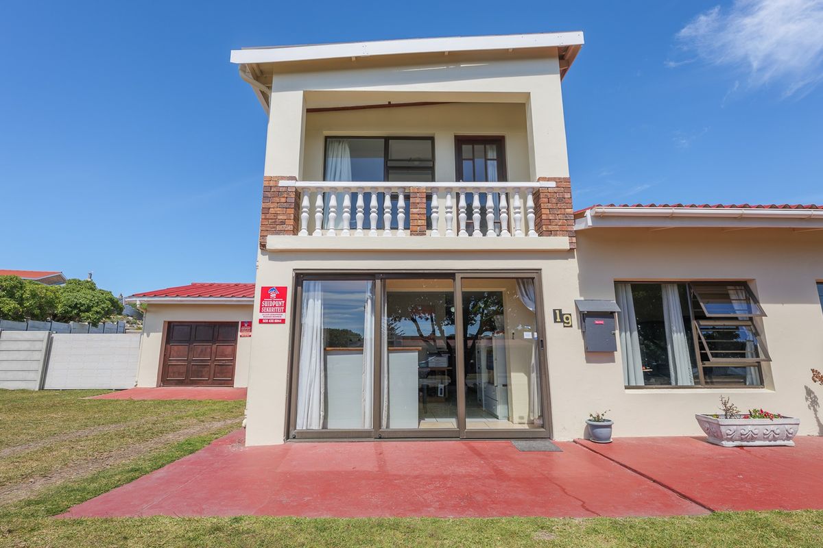 Rear view of a two-story house featuring a ground-level patio, sliding glass doors, and an upper-level balcony with a decorative balustrade.