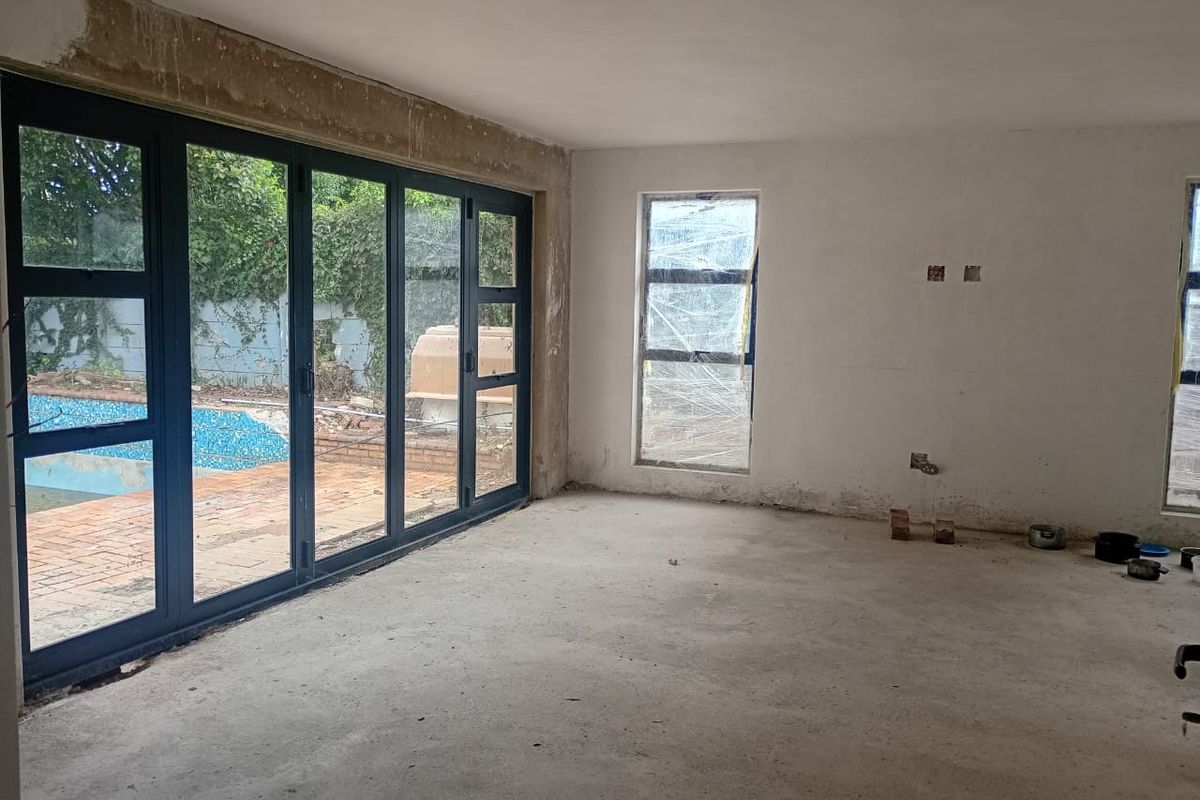 An unfinished living area featuring large aluminium stacker doors opening to a pool area, with raw concrete floors and unpainted plastered walls.