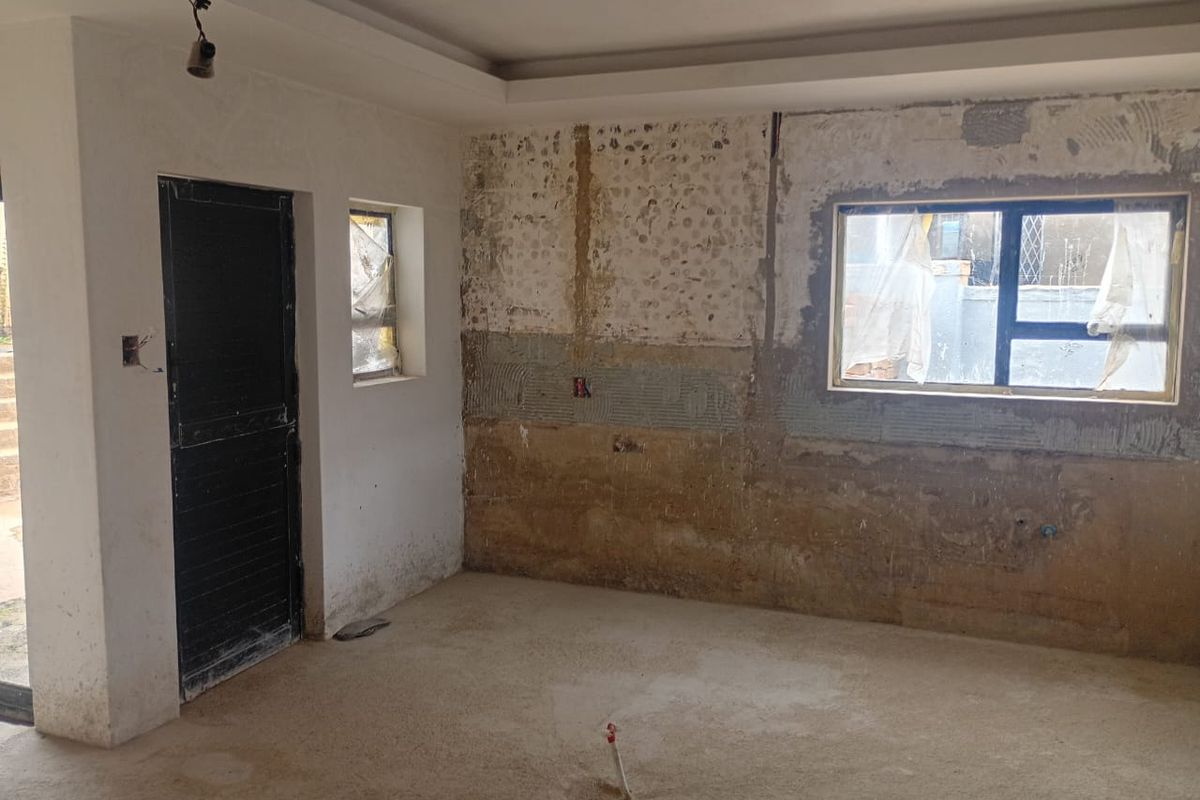 An unfinished kitchen space currently under renovation, featuring exposed wall surfaces, aluminium window frames, and plumbing rough-in, ready for final finishes and cabinetry installation.