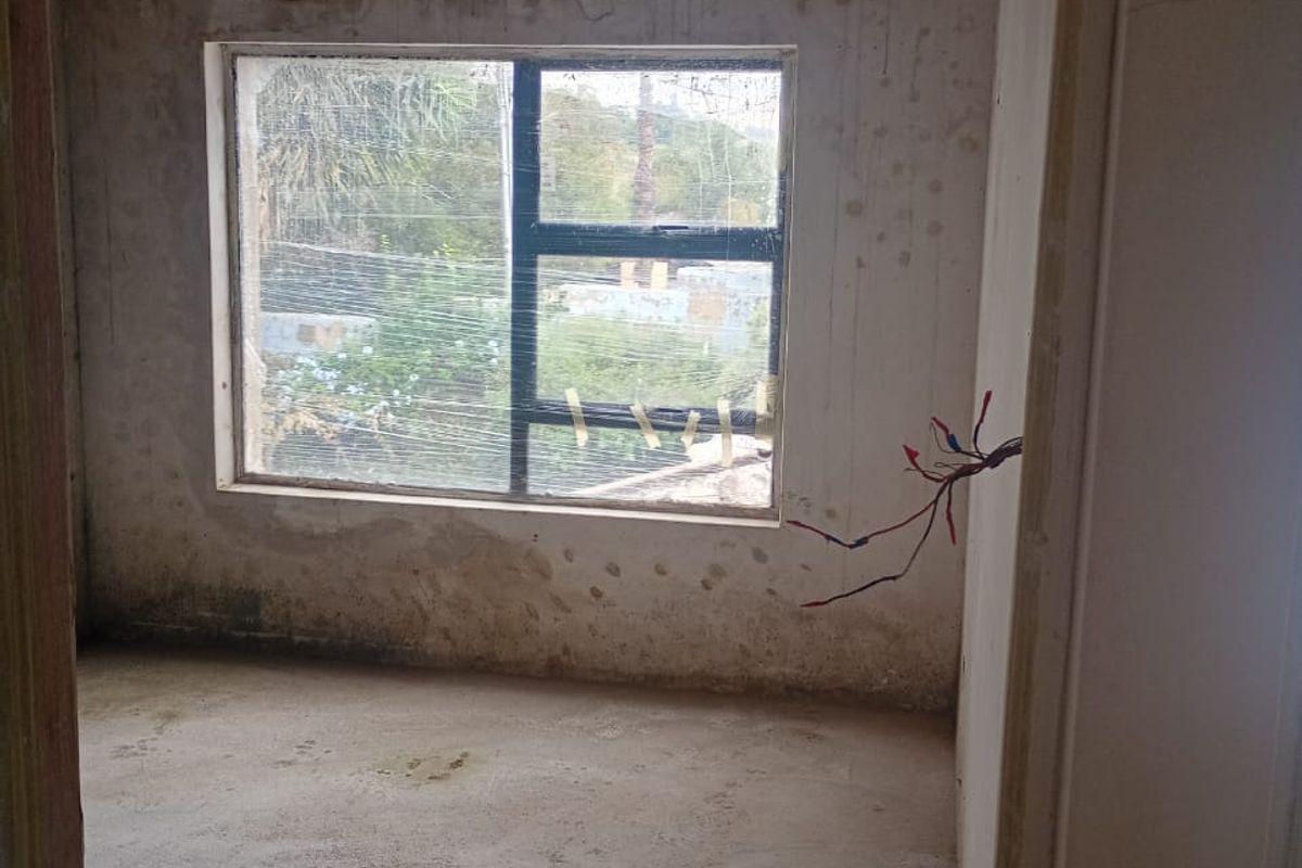 An unfinished bedroom space in shell condition, featuring exposed ceiling joists, raw concrete flooring, and exposed electrical wiring, ready for renovation.