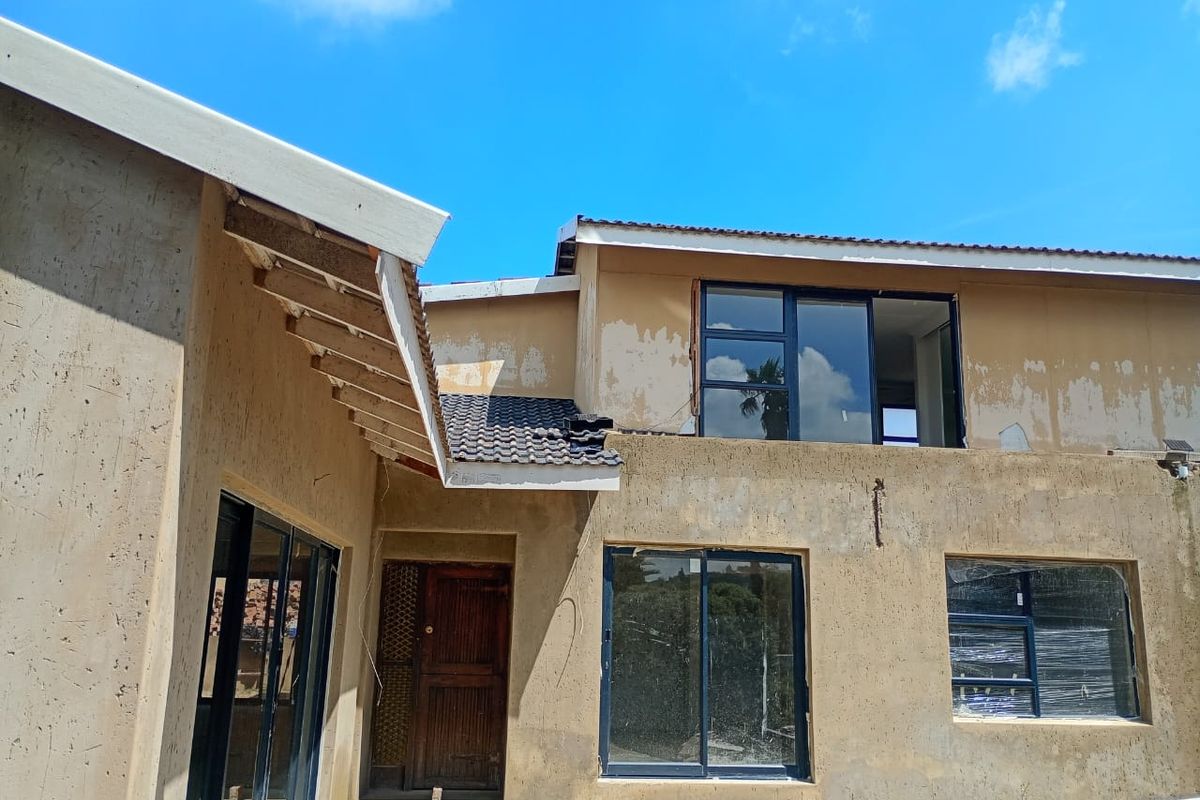 Rear elevation of a house under construction featuring aluminium sliding doors, timber entrance door, and unfinished exterior plasterwork.