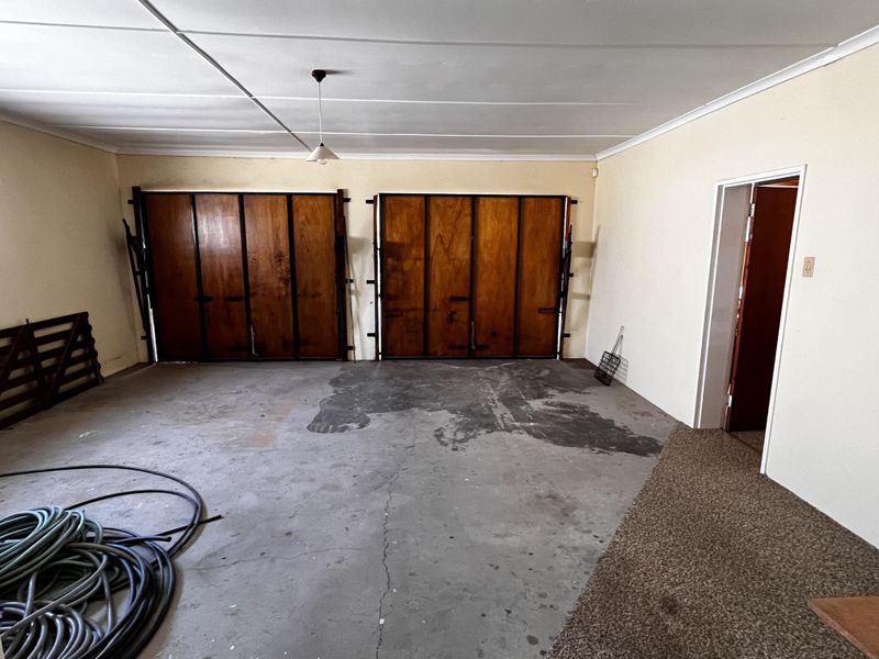 Spacious double garage featuring wooden tilt-up doors and concrete flooring, providing ample storage or parking space.