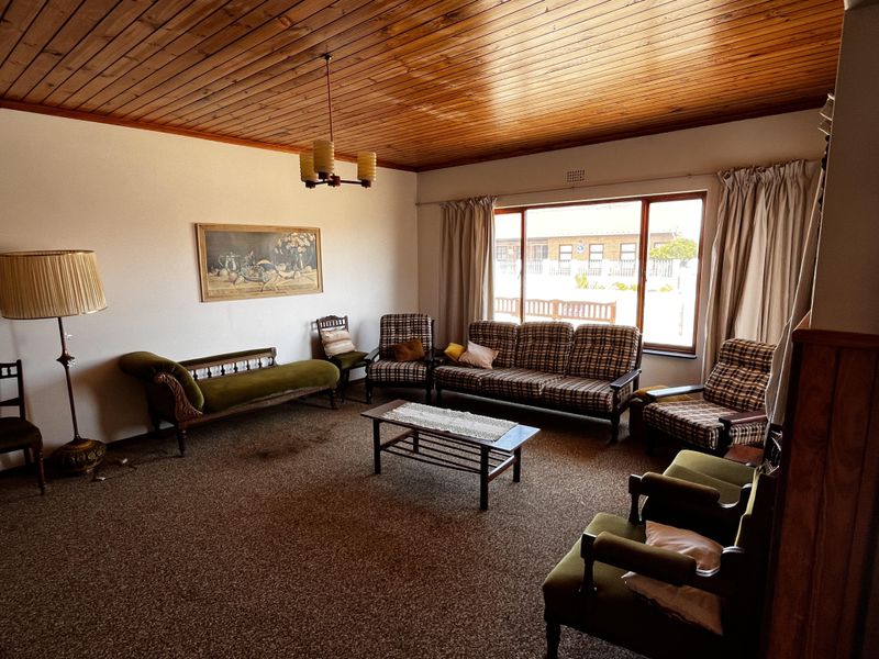 A spacious living room featuring a warm timber tongue and groove ceiling, large picture window, and carpeted flooring.