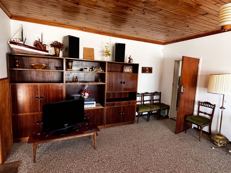 A living room featuring a timber-clad ceiling, fitted wooden wall cabinetry, and carpeted flooring.
