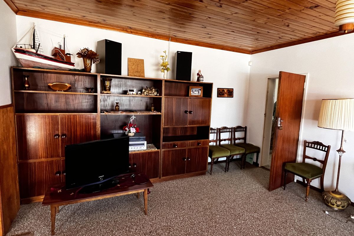 A living room featuring a timber-clad ceiling, fitted wooden wall cabinetry, and carpeted flooring.