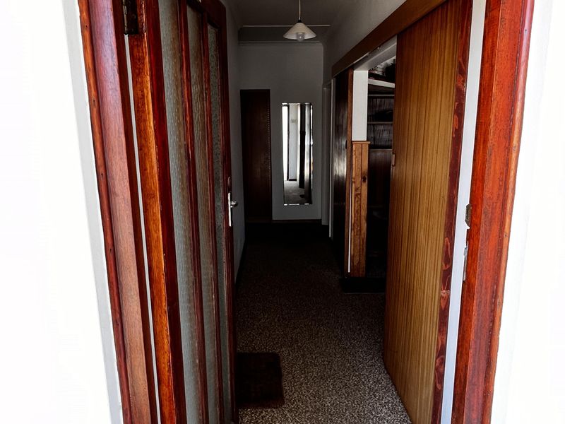 A narrow interior hallway featuring timber door frames, a sliding wooden door, and carpeted flooring, leading to further rooms within the property.