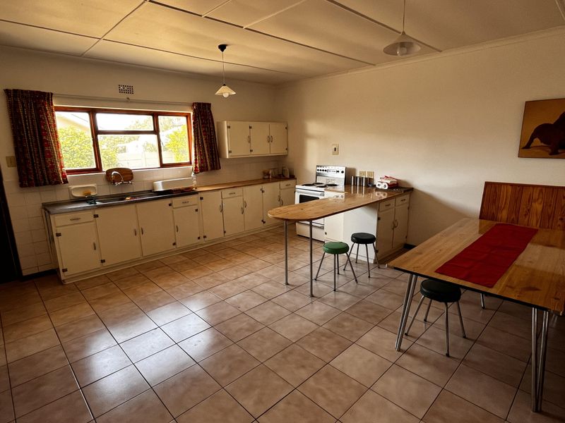 A spacious, dated kitchen featuring original cabinetry, a breakfast bar, tiled flooring, and a functional layout with a built-in sink and stove area.