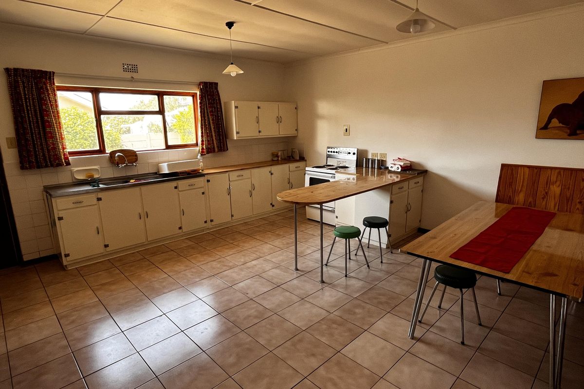 A spacious, dated kitchen featuring original cabinetry, a breakfast bar, tiled flooring, and a functional layout with a built-in sink and stove area.