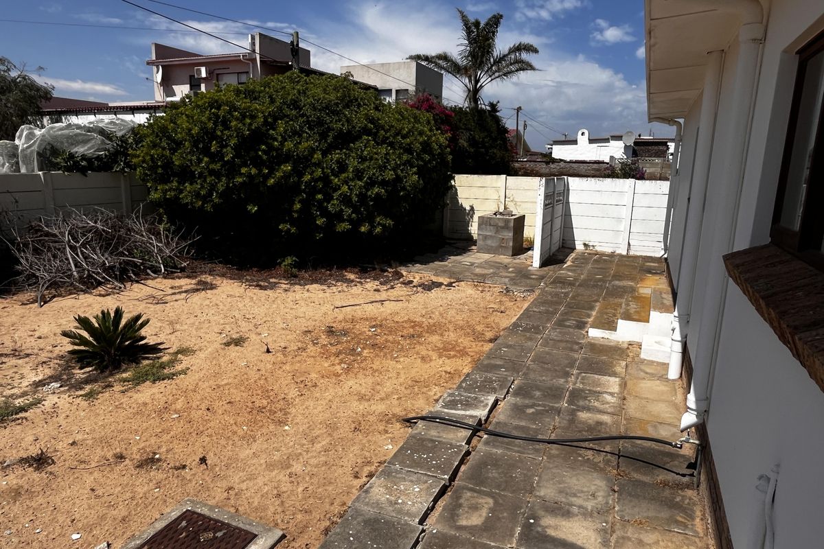 Rear garden area featuring a paved patio, built-in braai, and precast boundary walling, requiring landscaping and maintenance to improve the outdoor space.