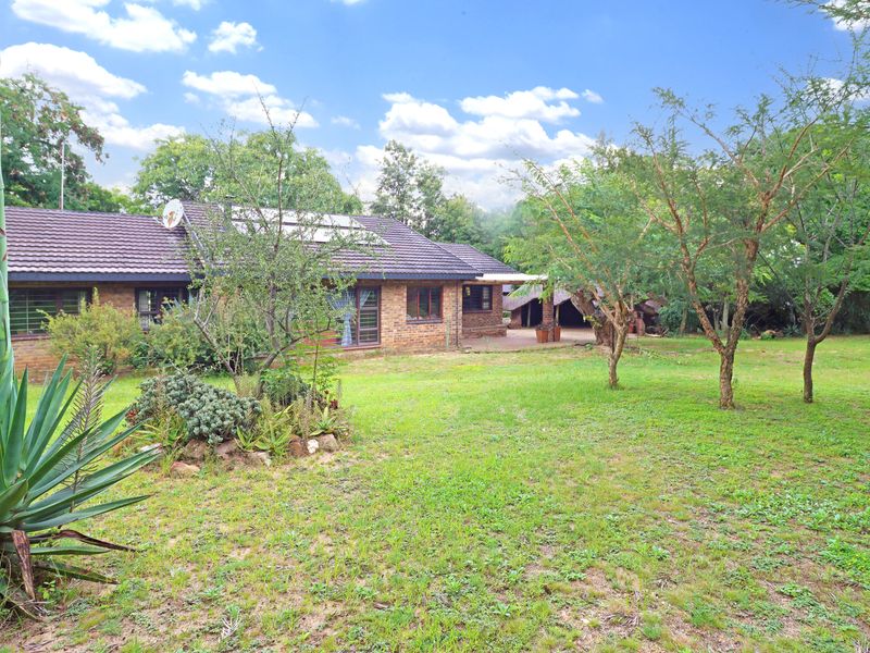 Rear view of a brick farmhouse featuring a tiled roof, solar water heating system, and a covered patio area overlooking a spacious garden.