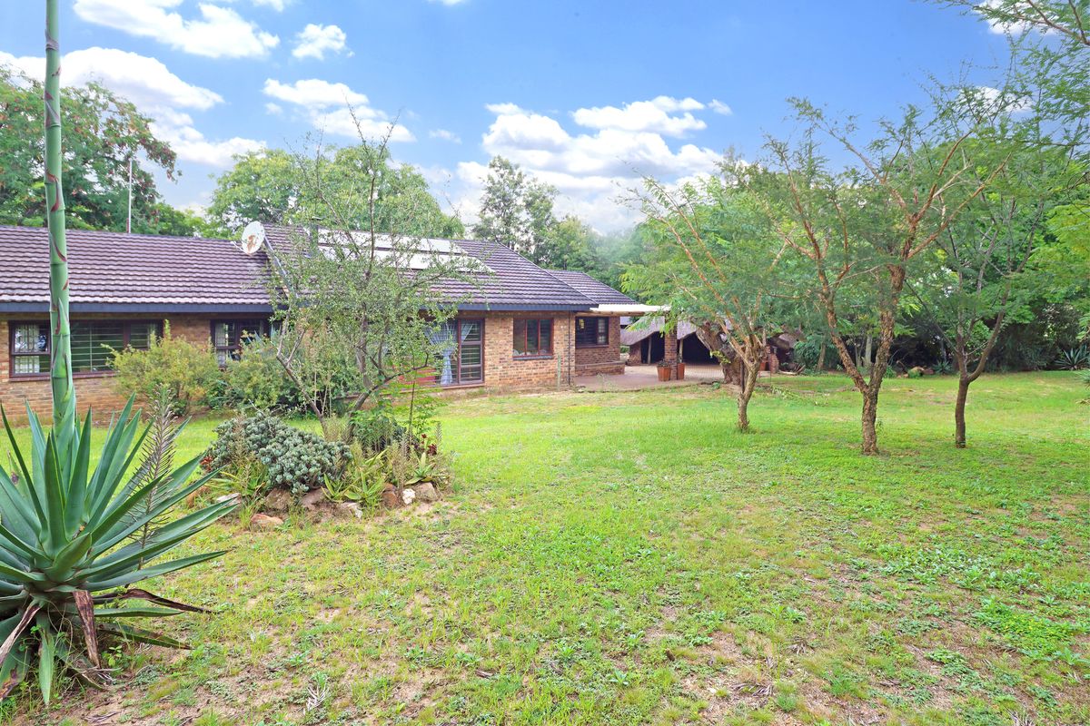 Rear view of a brick farmhouse featuring a tiled roof, solar water heating system, and a covered patio area overlooking a spacious garden.