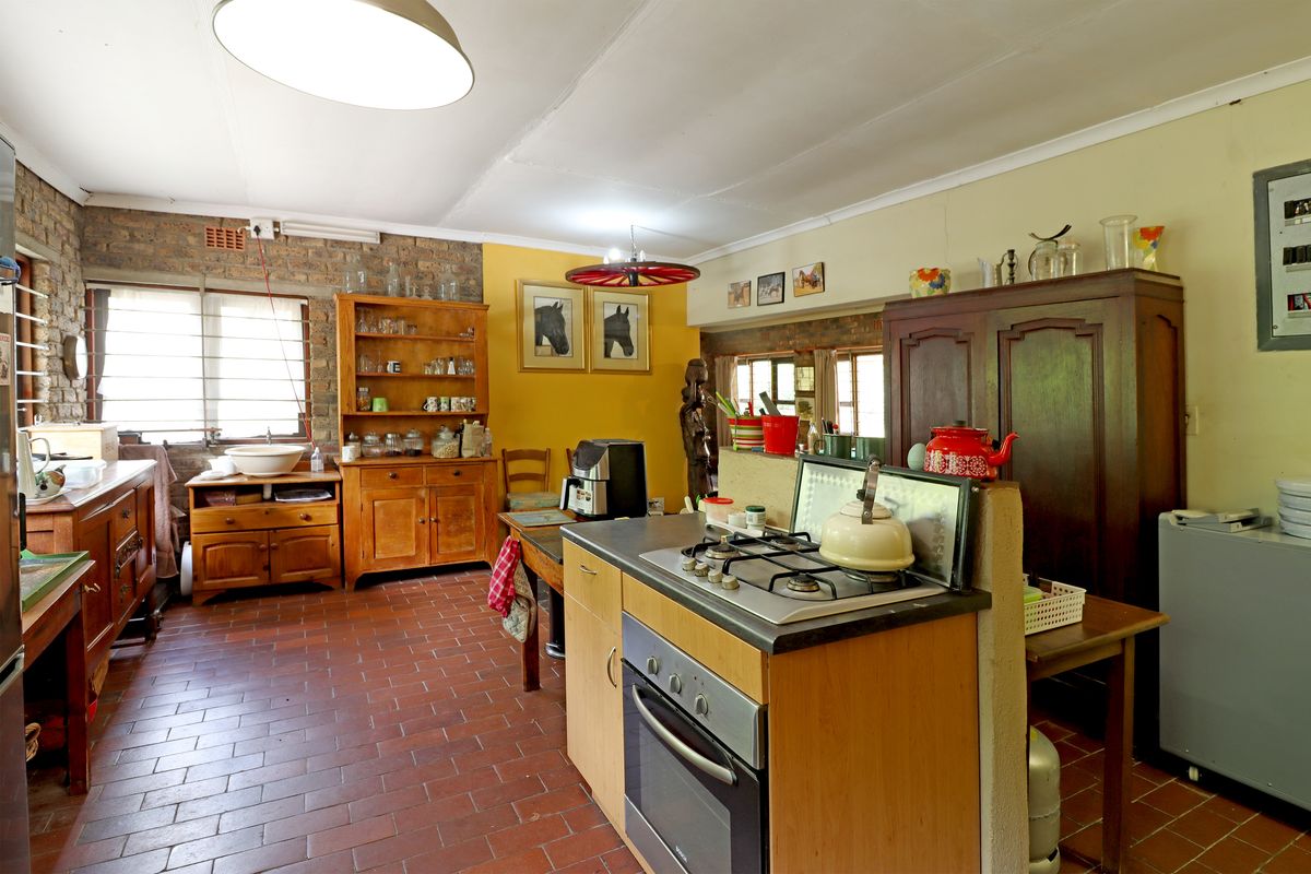 A rustic farmhouse kitchen featuring a brick accent wall, tiled flooring, and a central island with a built-in gas hob and oven.