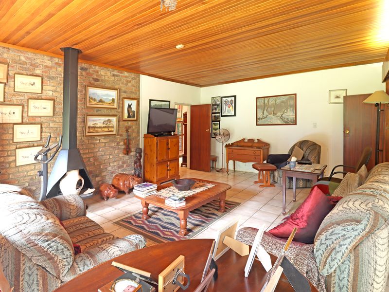 A living room featuring a prominent exposed brick wall, a freestanding fireplace, and a warm wood-panelled ceiling with tiled flooring throughout.