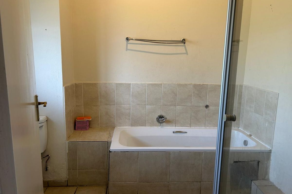 A functional bathroom featuring a built-in bathtub, tiled surround, and a separate shower enclosure, offering a blank canvas for potential renovation and modernization.