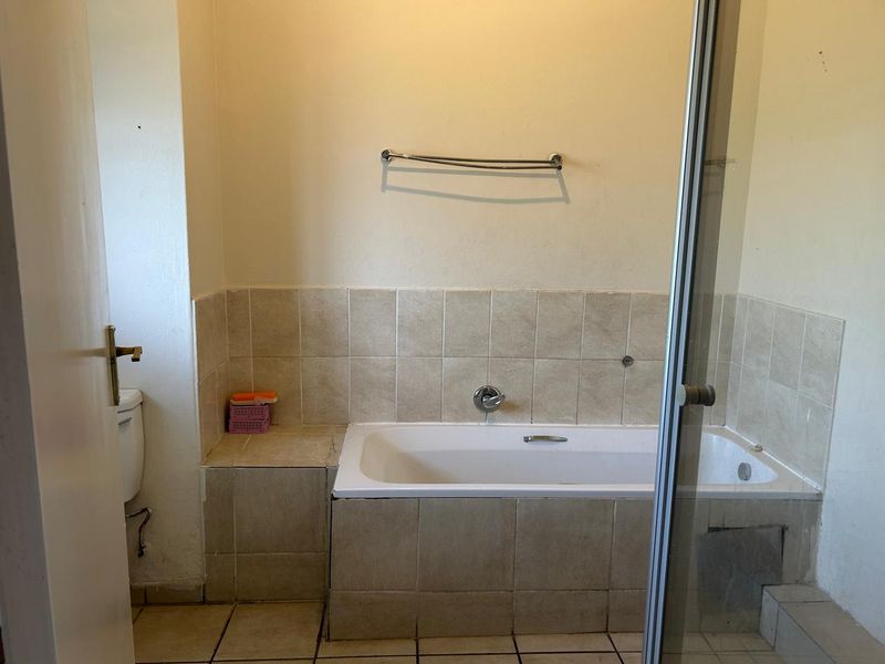 A functional bathroom featuring a built-in bathtub, tiled surround, and a separate shower enclosure, offering a blank canvas for potential renovation and modernization.