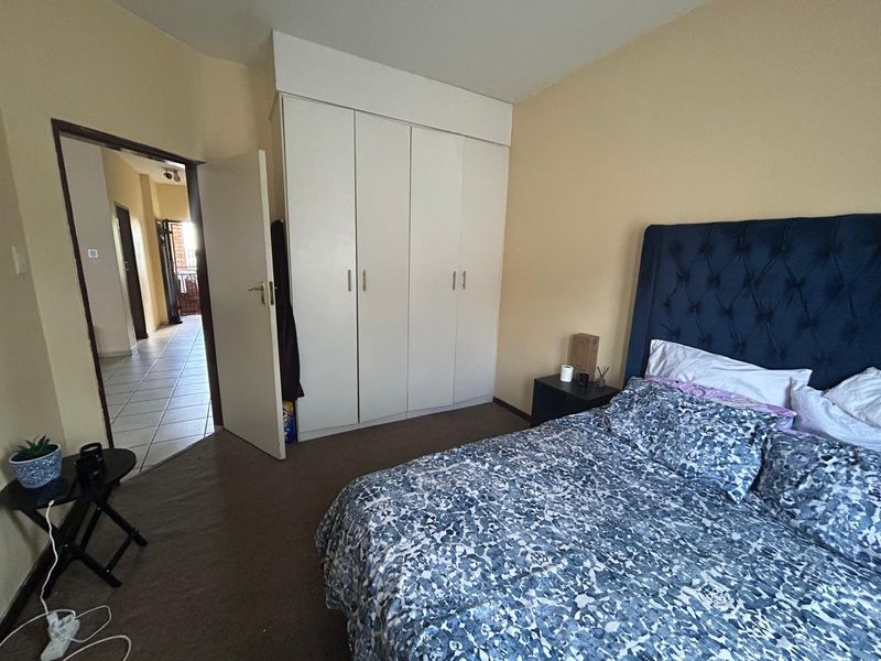A functional bedroom featuring built-in cupboards and carpeted flooring, with direct access to the hallway.