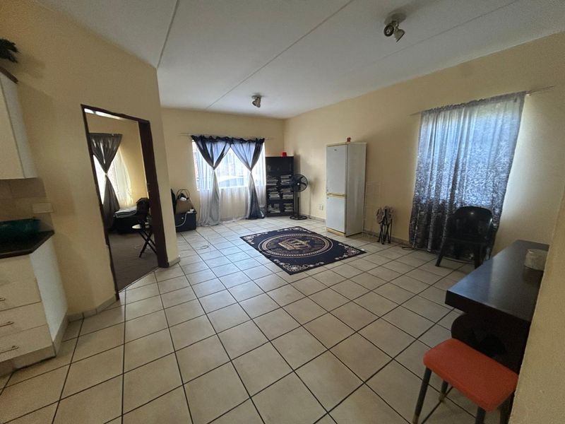Open plan living area featuring neutral wall tones and tiled flooring, providing a versatile space with direct access to an adjoining room.