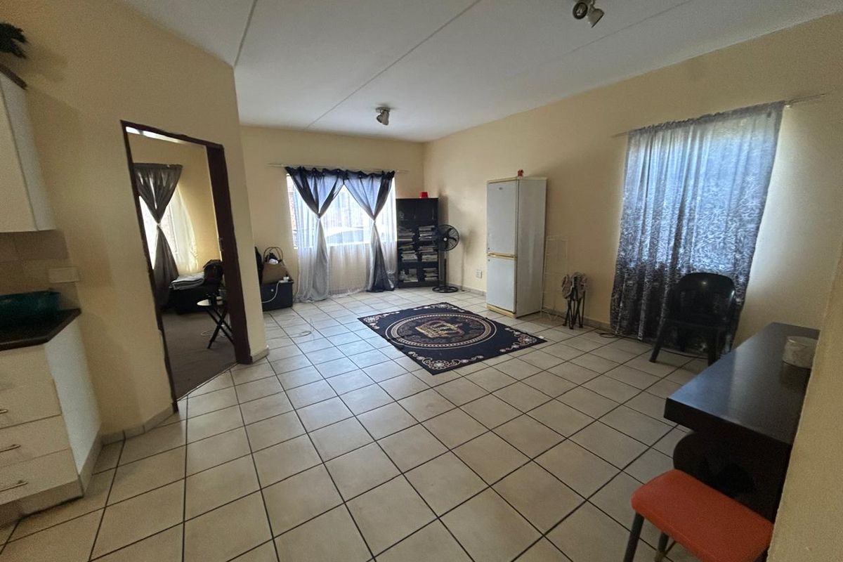 Open plan living area featuring neutral wall tones and tiled flooring, providing a versatile space with direct access to an adjoining room.
