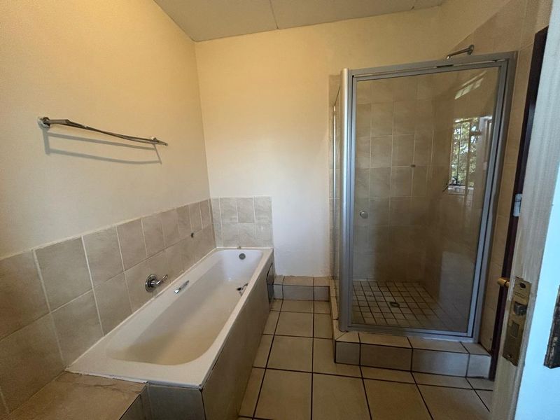A functional bathroom featuring a built-in bathtub, a separate shower enclosure with glass door, and neutral tiled finishes throughout.