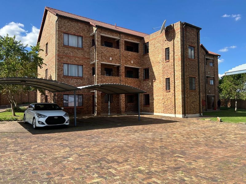 A multi-story face brick apartment building featuring a paved driveway and covered carport parking spaces.