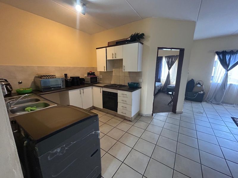Open-plan kitchen area featuring built-in cabinetry, tiled flooring, and integrated cooking appliances, leading into an adjacent living space.
