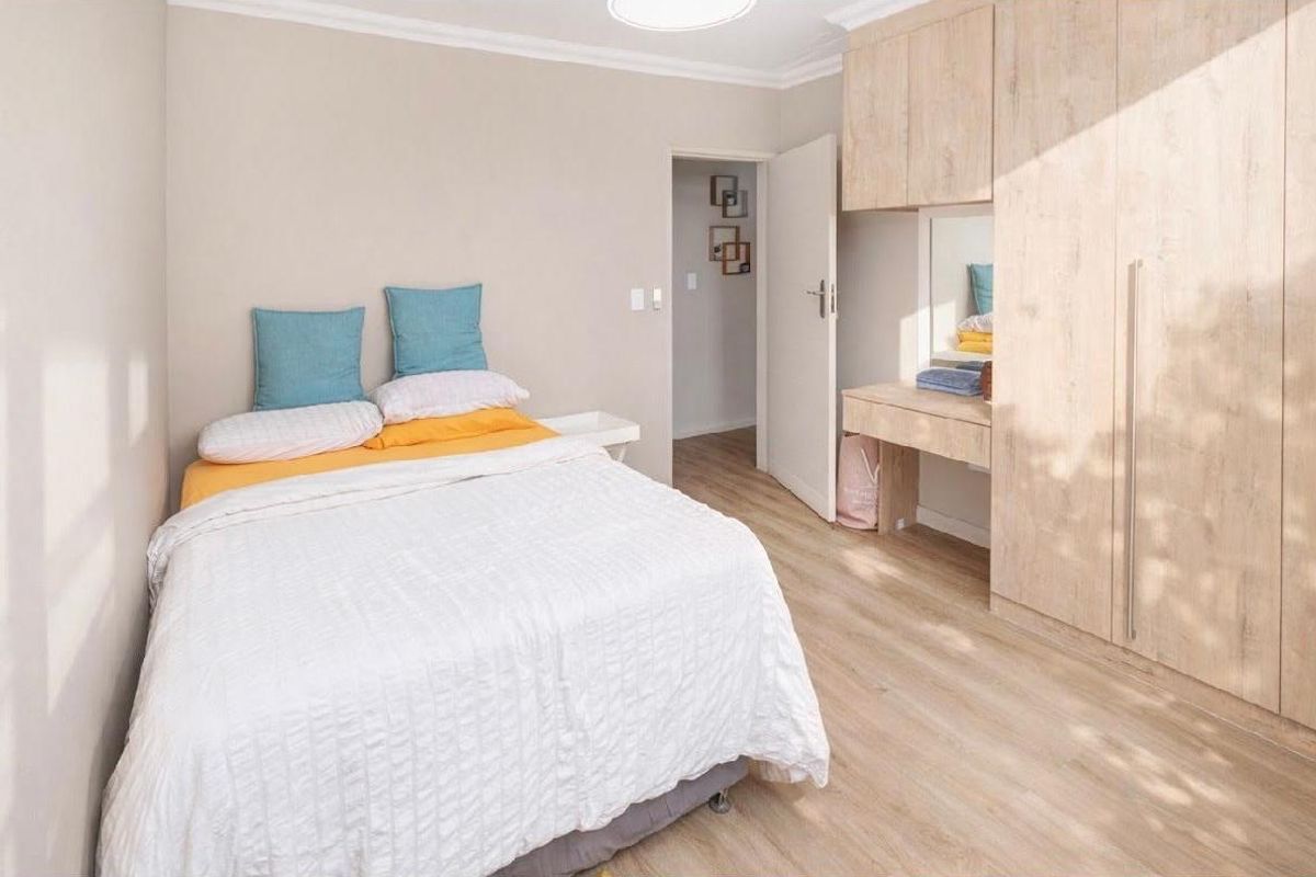 A well-maintained bedroom featuring light wood-look laminate flooring, built-in cabinetry with an integrated vanity, and neutral wall finishes.
