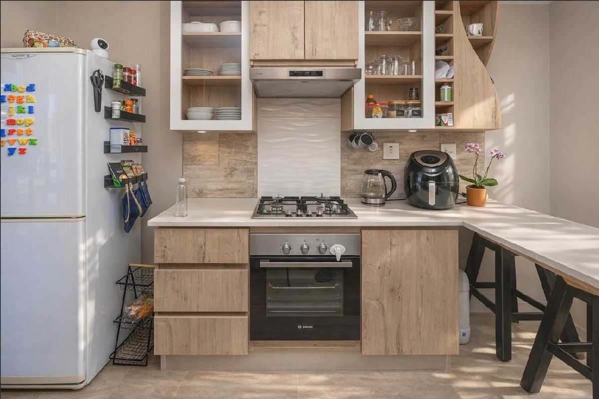A modern, well-maintained kitchen featuring light wood-finish cabinetry, a gas hob, built-in oven, extractor fan, and stone countertops with a breakfast nook.
