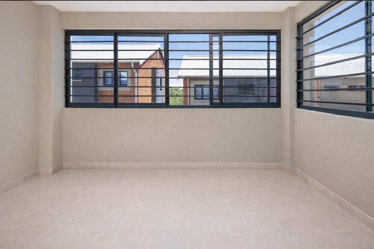 A bright, empty living area featuring neutral tiled flooring and large sliding windows fitted with security bars, offering a clean and versatile space.