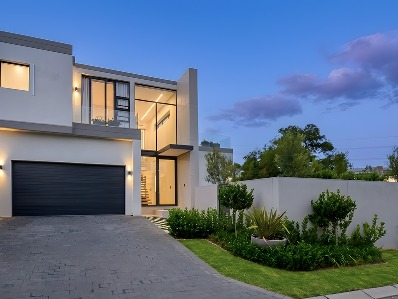 Modern contemporary townhouse featuring a double garage, paved driveway, and landscaped garden with elegant exterior lighting at dusk.