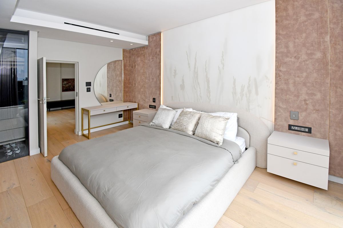 Modern bedroom featuring timber flooring, recessed ceiling lighting, integrated wall accents, and a built-in vanity area with a sleek, contemporary finish.