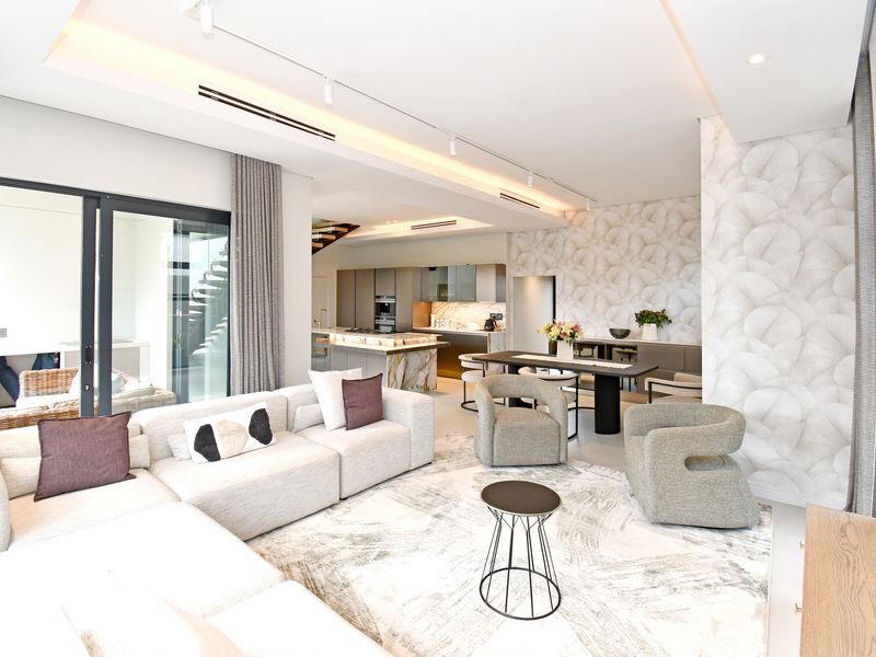 Modern open-plan living area featuring a sleek kitchen with stone island, recessed lighting, ducted air conditioning, and seamless access to the outdoor patio.