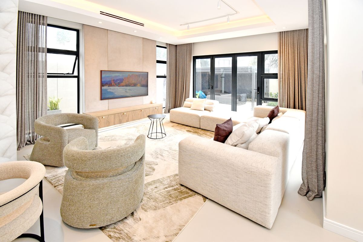 A modern, well-lit living room featuring large windows, bi-fold doors leading to the patio, and custom built-in cabinetry with a neutral color palette.