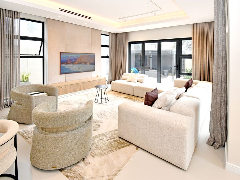 A modern, well-lit living room featuring large windows, bi-fold doors leading to the patio, and custom built-in cabinetry with a neutral color palette.