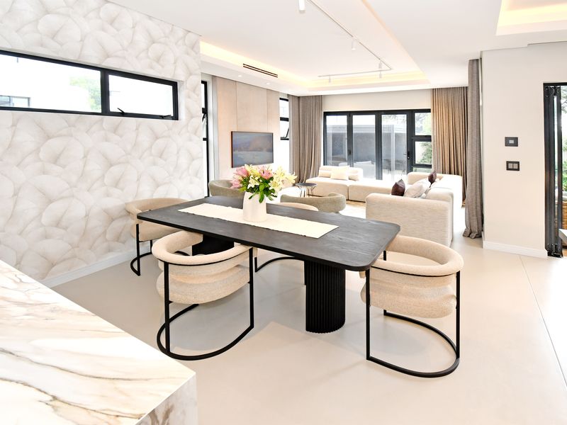 Modern open-plan living and dining area featuring high-end finishes, recessed ceiling lighting, and seamless access to the outdoor patio through black aluminium stacker doors.