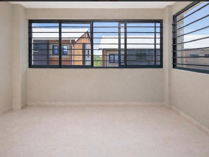 A bright, empty living area featuring neutral tiled flooring and large sliding windows fitted with security bars, offering a clean and versatile space.