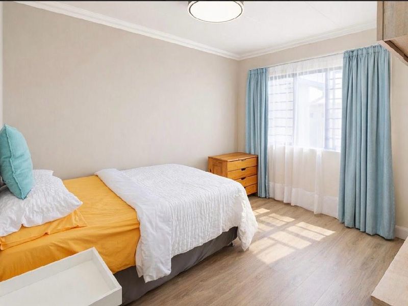 A well-lit bedroom featuring durable laminate flooring, neutral wall tones, and a window fitted with security bars.